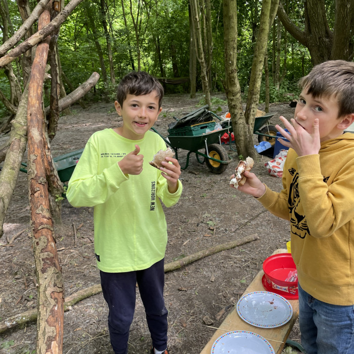 Two boys are enjoying eating snakcs they have cooked on an open fire