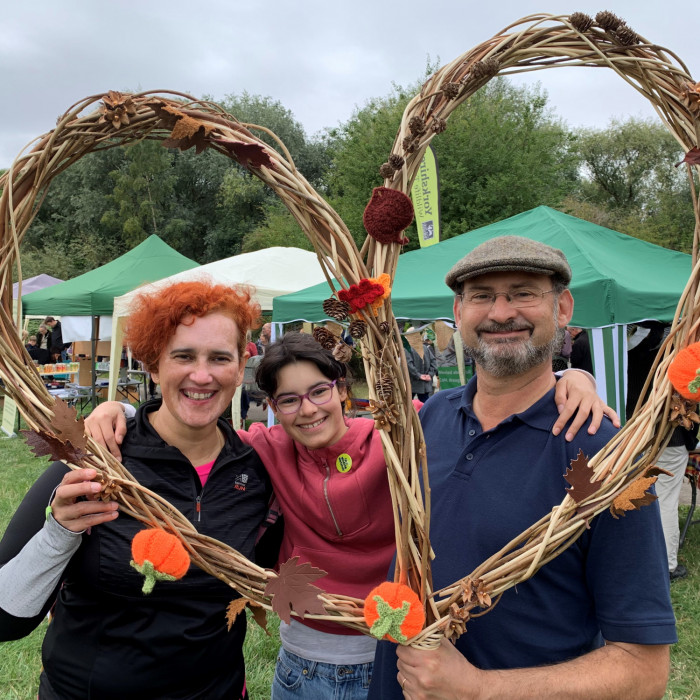 A family (woman, a teenager and a man) at the autumn fayre holding a heart-shaped frame made of willow