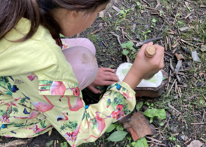 A child is making leaf art using cotton and a wooden tool.