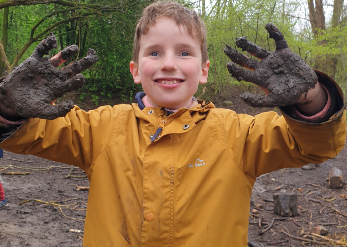 A smiling boy in the woodland area with very muddy hands