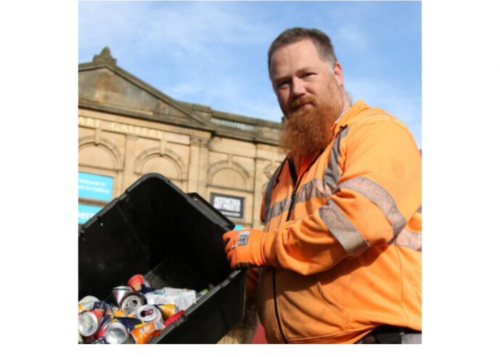 Stuart Watling a portly white red haired man with long beard looking into the camera he is tipping a box of aluminium into a bin