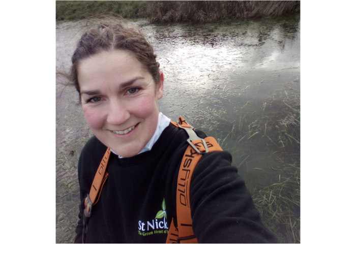 Nicola Ward is a woman with long dark hair tied back, she is smiling at the camera and wearing waders standing next to some water