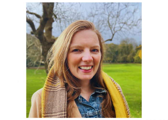 Vicky, a white woman with long straight ginger hair, smiling at the camera in a field