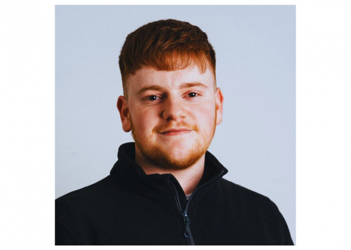 Harrison - a young man with ginger hair and stubble looking directly at the camera, in front of a plain background