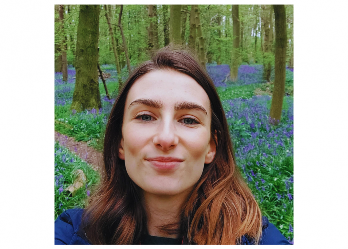 Catriona, a young woman with long straight brown hair and blue eyes, in a woodland with bluebells